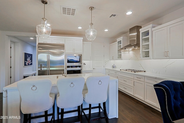 kitchen with built in appliances, wall chimney range hood, pendant lighting, and backsplash