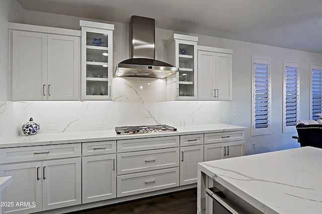 kitchen featuring stainless steel gas stovetop, white cabinetry, tasteful backsplash, light stone countertops, and wall chimney exhaust hood