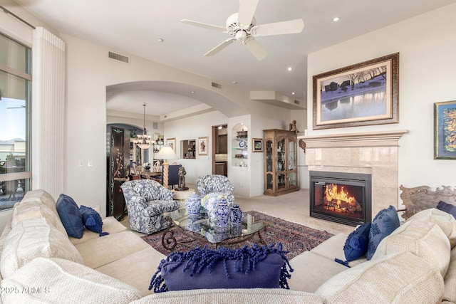 living area with ceiling fan with notable chandelier, visible vents, carpet floors, arched walkways, and a tiled fireplace