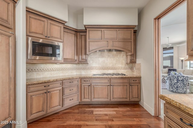 kitchen featuring light stone countertops, built in microwave, stainless steel gas cooktop, decorative backsplash, and light wood-style floors