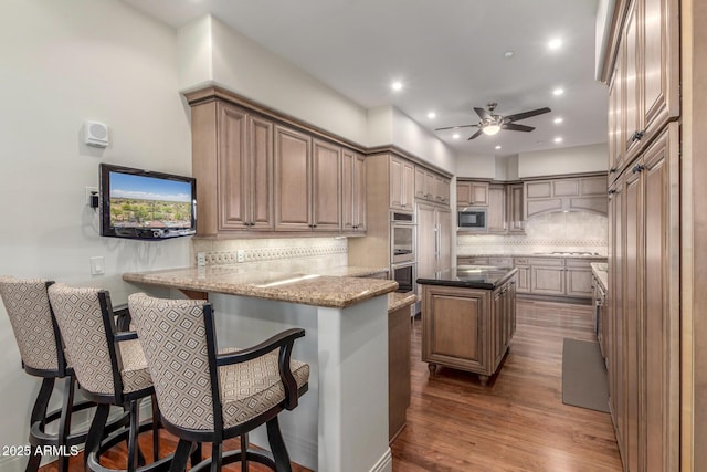 kitchen featuring a peninsula, a kitchen bar, double oven, tasteful backsplash, and black microwave