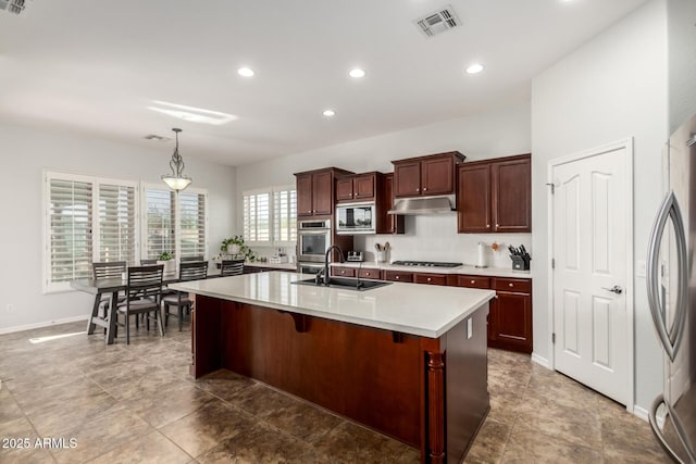 kitchen with appliances with stainless steel finishes, a kitchen breakfast bar, sink, decorative light fixtures, and a center island with sink