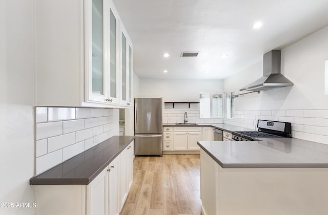 kitchen with wall chimney range hood, sink, stainless steel appliances, white cabinets, and light wood-type flooring