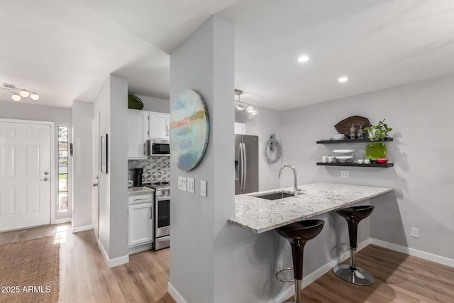 kitchen featuring a breakfast bar area, a sink, white cabinets, appliances with stainless steel finishes, and tasteful backsplash