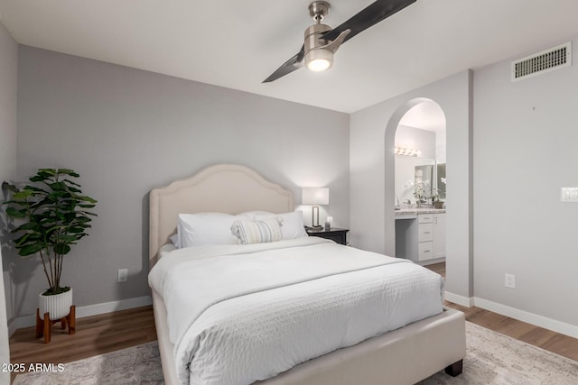 bedroom featuring baseboards, visible vents, arched walkways, wood finished floors, and ensuite bathroom