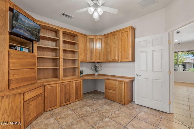 unfurnished office featuring light tile patterned floors, built in desk, and ceiling fan