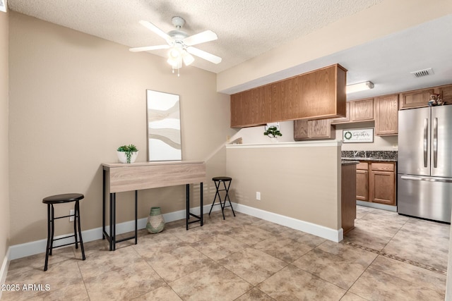 kitchen with visible vents, a ceiling fan, a textured ceiling, freestanding refrigerator, and brown cabinetry