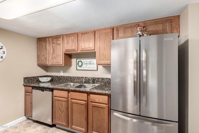 kitchen featuring a sink, dark countertops, a textured ceiling, stainless steel appliances, and baseboards