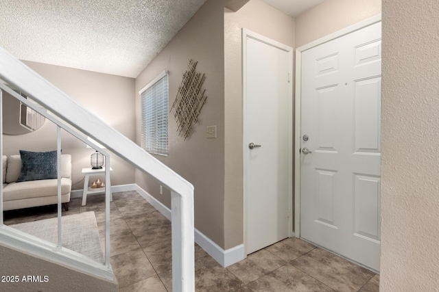 tiled foyer entrance featuring a textured wall, baseboards, and a textured ceiling