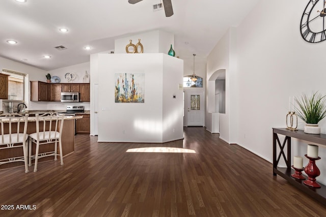 kitchen with stainless steel appliances, lofted ceiling, dark hardwood / wood-style flooring, ceiling fan, and a kitchen breakfast bar