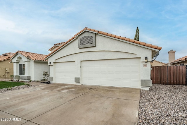 mediterranean / spanish-style home featuring concrete driveway, a tile roof, an attached garage, fence, and stucco siding