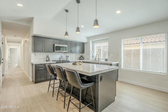 kitchen featuring light countertops, stainless steel microwave, gray cabinetry, decorative backsplash, and a kitchen breakfast bar