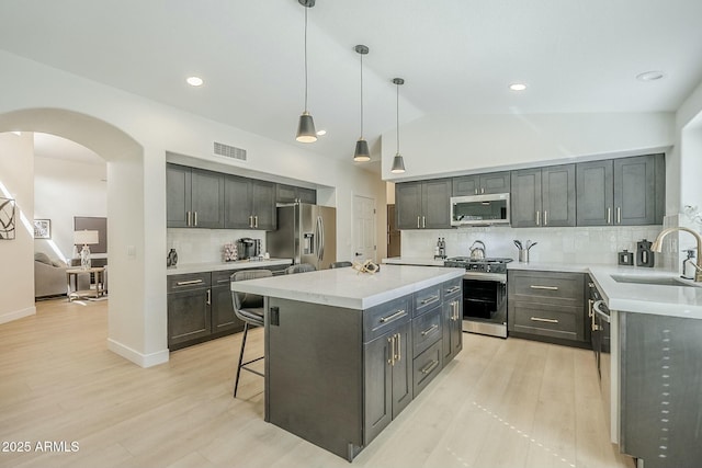 kitchen with arched walkways, a sink, visible vents, appliances with stainless steel finishes, and a center island