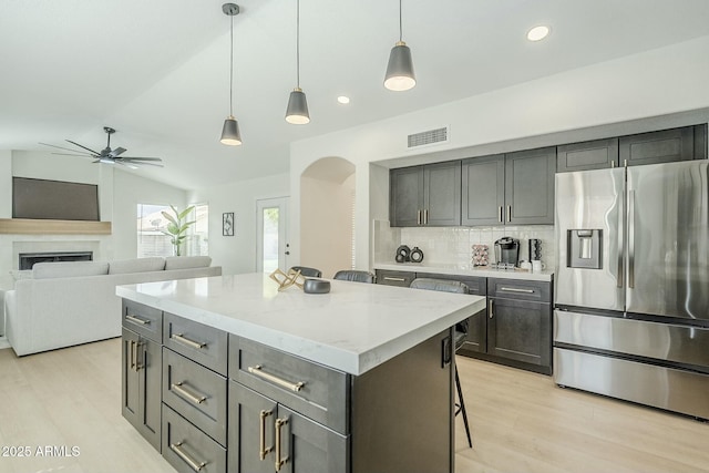 kitchen with stainless steel fridge with ice dispenser, lofted ceiling, light wood-style flooring, a kitchen island, and backsplash