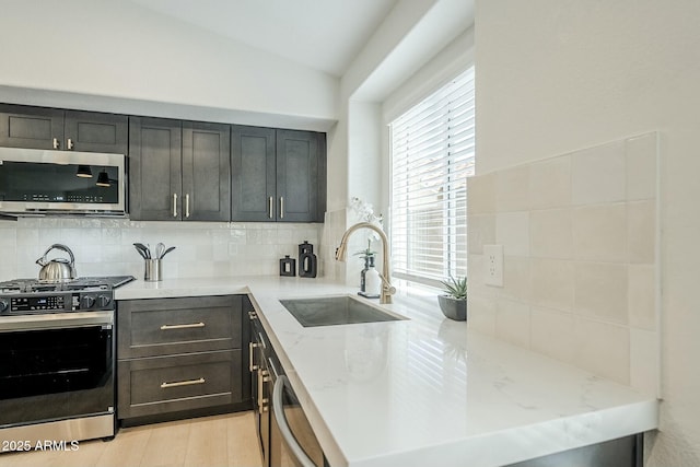 kitchen with stainless steel appliances, a sink, decorative backsplash, light stone countertops, and light wood finished floors