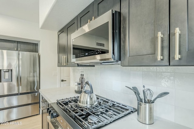 kitchen with light stone countertops, tasteful backsplash, appliances with stainless steel finishes, and light wood-style flooring