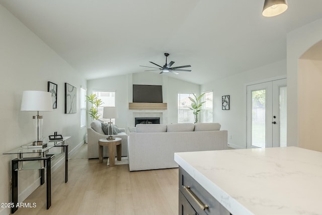 living area featuring a ceiling fan, lofted ceiling, light wood-style flooring, a healthy amount of sunlight, and a fireplace