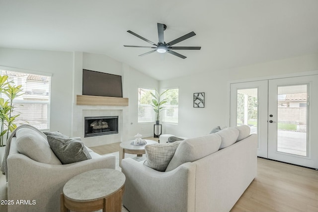 living area featuring french doors, lofted ceiling, a ceiling fan, light wood-type flooring, and a tile fireplace