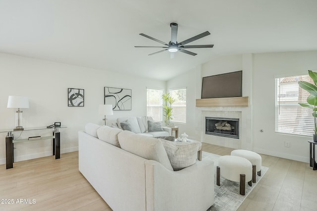 living room featuring lofted ceiling, light wood finished floors, a tile fireplace, and a ceiling fan