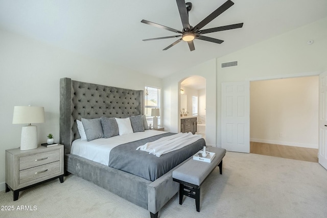 bedroom featuring arched walkways, lofted ceiling, light colored carpet, visible vents, and ensuite bath