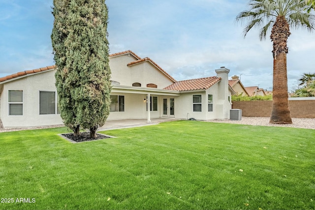 back of property with a yard, a chimney, a patio, stucco siding, and central AC