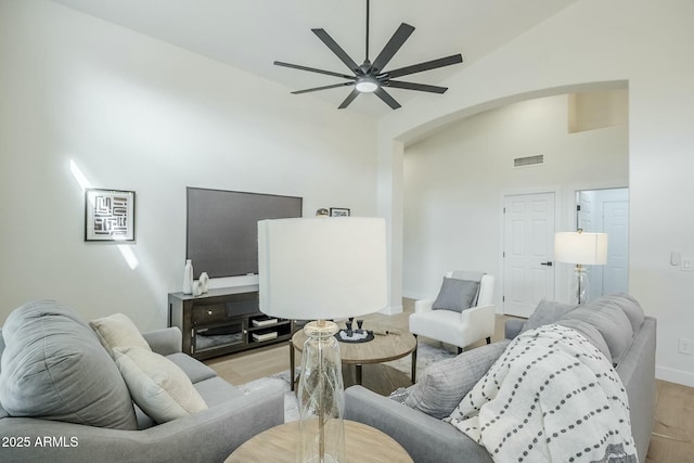 living room featuring baseboards, visible vents, a ceiling fan, light wood-style flooring, and high vaulted ceiling