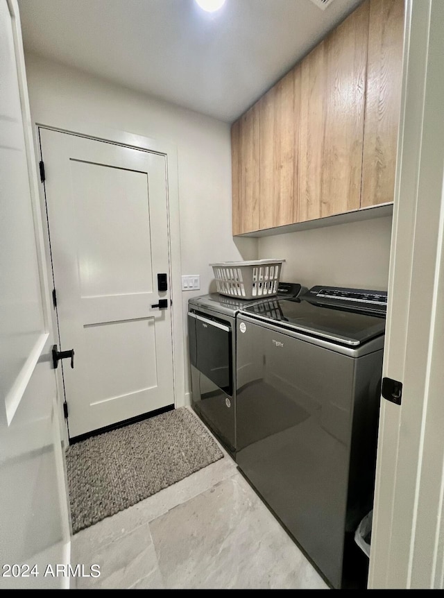 clothes washing area with cabinets, tile floors, and washer and clothes dryer