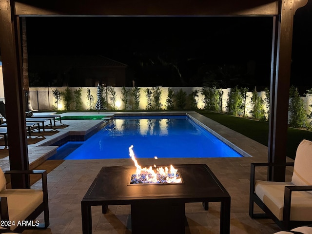 pool at night with a patio area and an outdoor fire pit