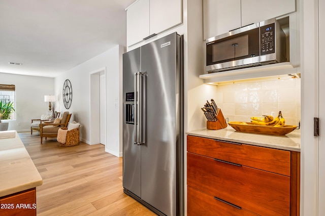 kitchen with stainless steel appliances, tasteful backsplash, light countertops, and white cabinets