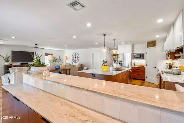 kitchen with brown cabinetry, visible vents, ceiling fan, open floor plan, and appliances with stainless steel finishes