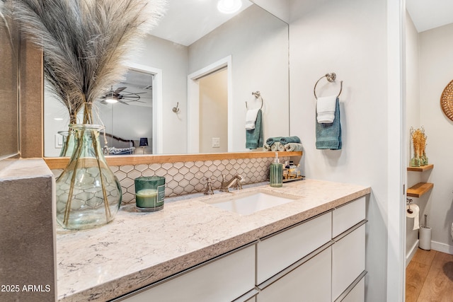 bathroom featuring baseboards, ceiling fan, vanity, wood finished floors, and backsplash