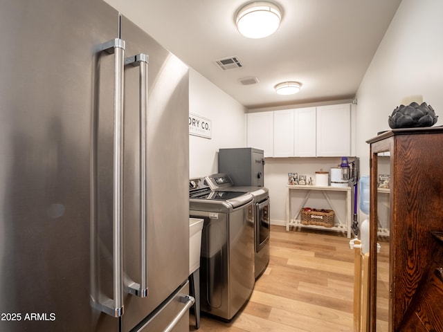 laundry area featuring washer and dryer, visible vents, light wood-style flooring, and cabinet space