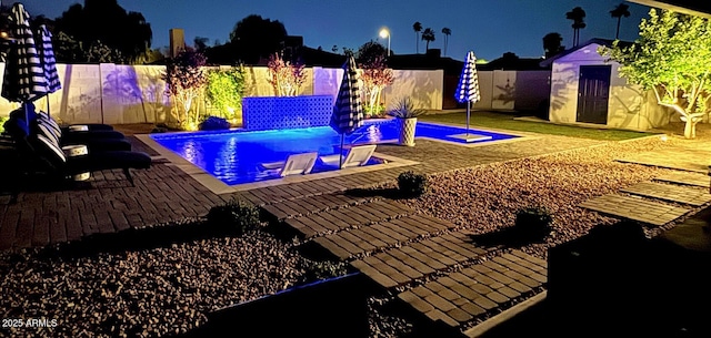 pool at night with a patio area, a storage shed, an outbuilding, a fenced backyard, and a fenced in pool