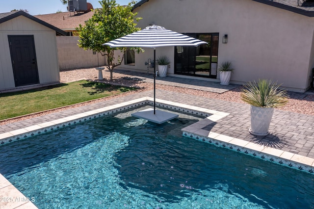 outdoor pool with an outbuilding, fence, a patio area, central AC unit, and a storage unit