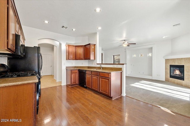 kitchen with ceiling fan, sink, black appliances, light hardwood / wood-style floors, and a tiled fireplace