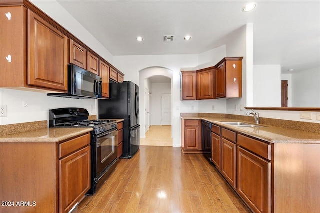 kitchen featuring light stone countertops, sink, kitchen peninsula, light hardwood / wood-style floors, and black appliances