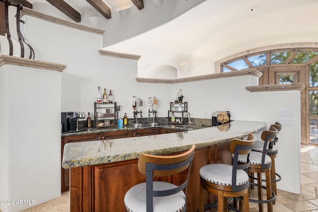 bar featuring dark stone countertops, sink, and beamed ceiling