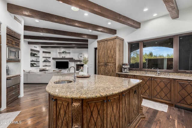 kitchen with a kitchen island with sink, sink, light stone countertops, and dark hardwood / wood-style floors