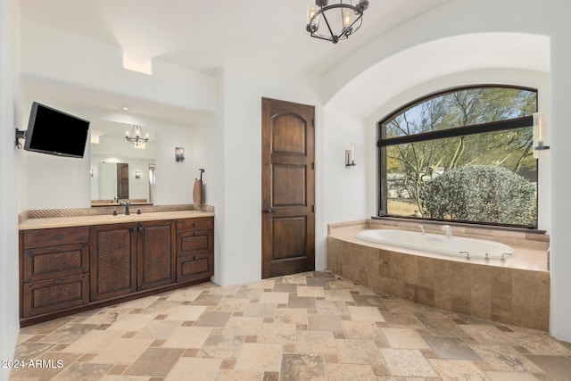 bathroom with vanity, a relaxing tiled tub, and an inviting chandelier