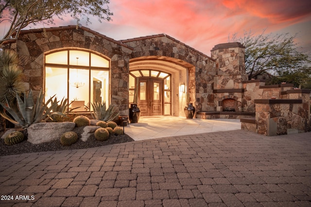 exterior entry at dusk featuring an outdoor stone fireplace and french doors