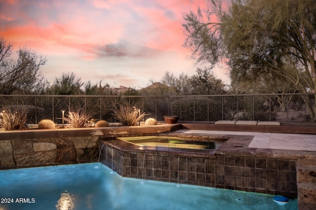 pool at dusk featuring pool water feature, a patio area, and an in ground hot tub