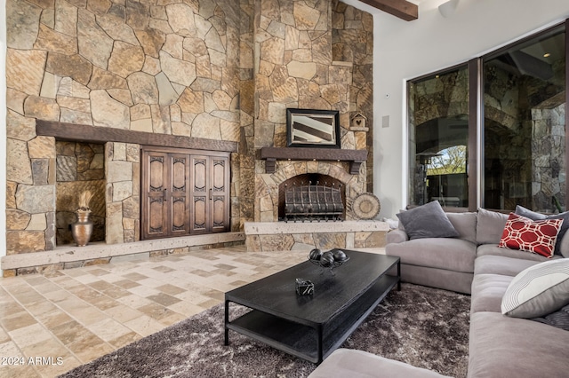 living room featuring beam ceiling and a stone fireplace