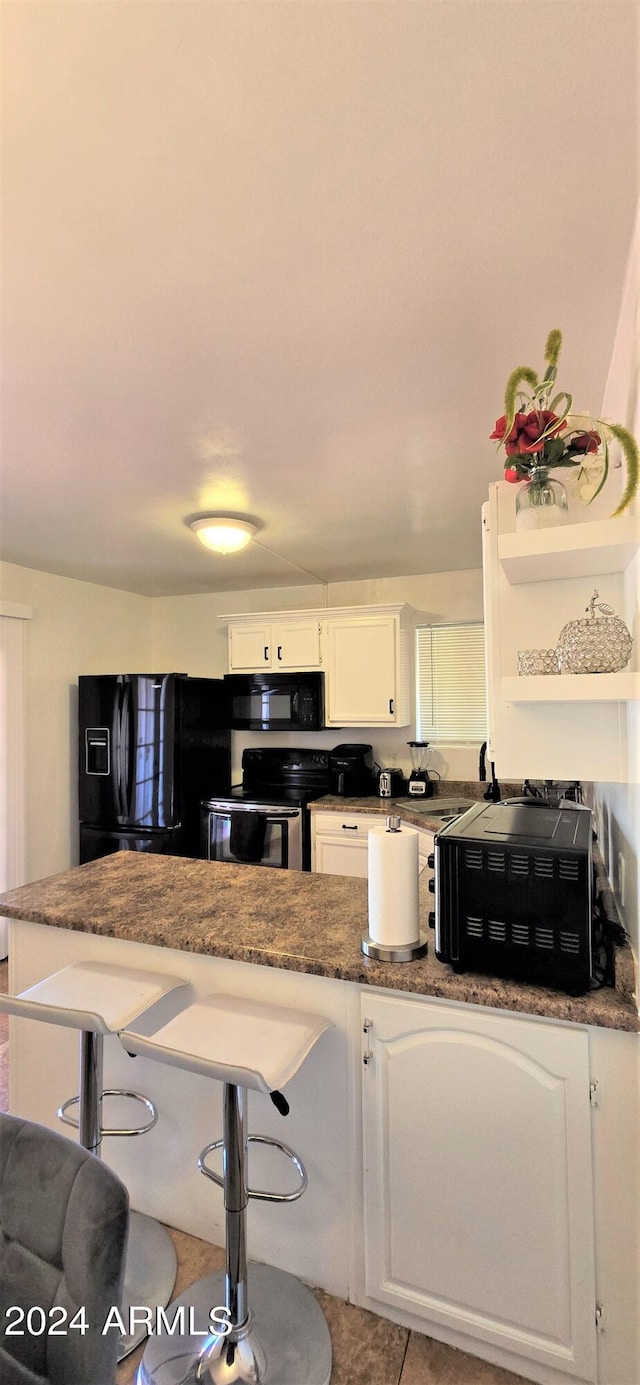 kitchen featuring white cabinetry, light tile patterned floors, black appliances, kitchen peninsula, and a breakfast bar area