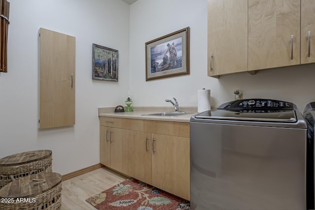 clothes washing area featuring light wood finished floors, baseboards, separate washer and dryer, cabinet space, and a sink