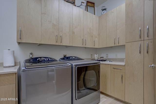 clothes washing area with washer and clothes dryer, cabinet space, and light wood-style floors