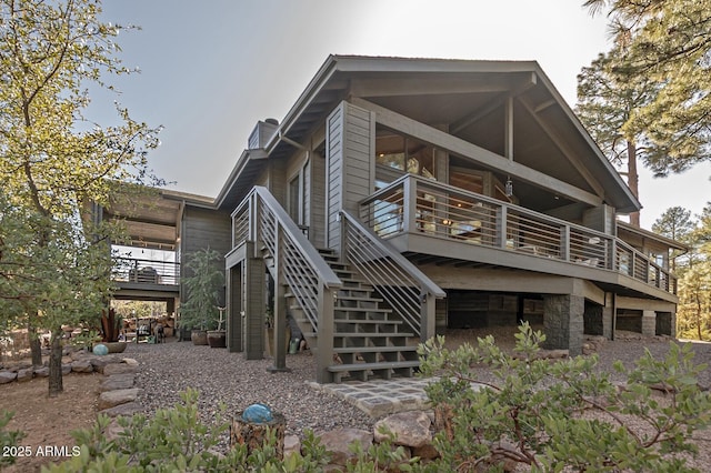 rear view of house featuring a deck, stairway, stone siding, and a chimney