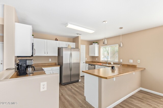 kitchen with pendant lighting, kitchen peninsula, appliances with stainless steel finishes, and light hardwood / wood-style flooring