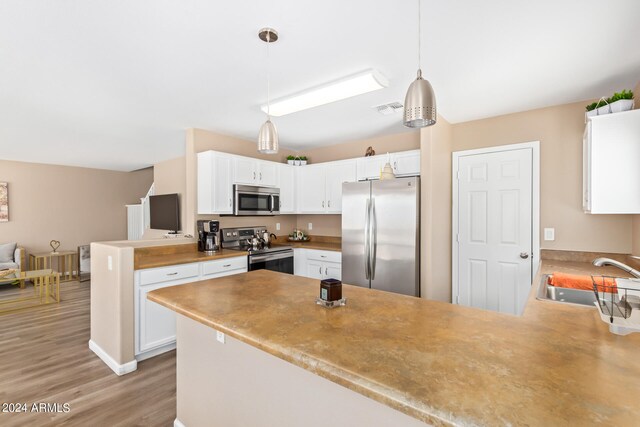 kitchen with appliances with stainless steel finishes, kitchen peninsula, light wood-type flooring, pendant lighting, and sink