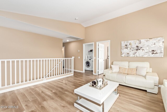 living room with washer / clothes dryer, vaulted ceiling, and light hardwood / wood-style flooring