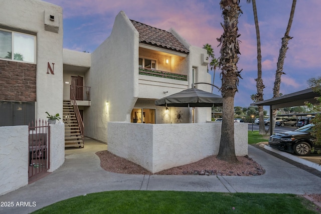 view of front of house with a balcony, stucco siding, stairs, a fenced front yard, and a tile roof